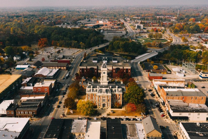 Aerial view of historic stone buildings surrounded by colorful fall foliage and urban roads.