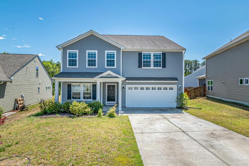 Modern two-story house with landscaped yard and large driveway under clear blue skies.