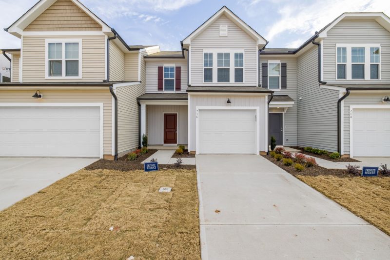 Contemporary suburban homes with garages and well-maintained lawns beneath a clear blue sky.