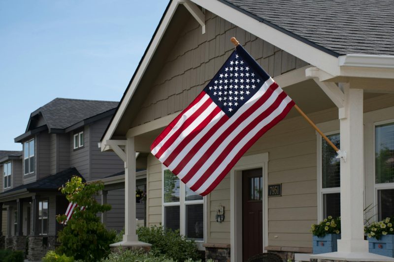 Vibrant American flag waving outside a stylish suburban house under clear daylight.